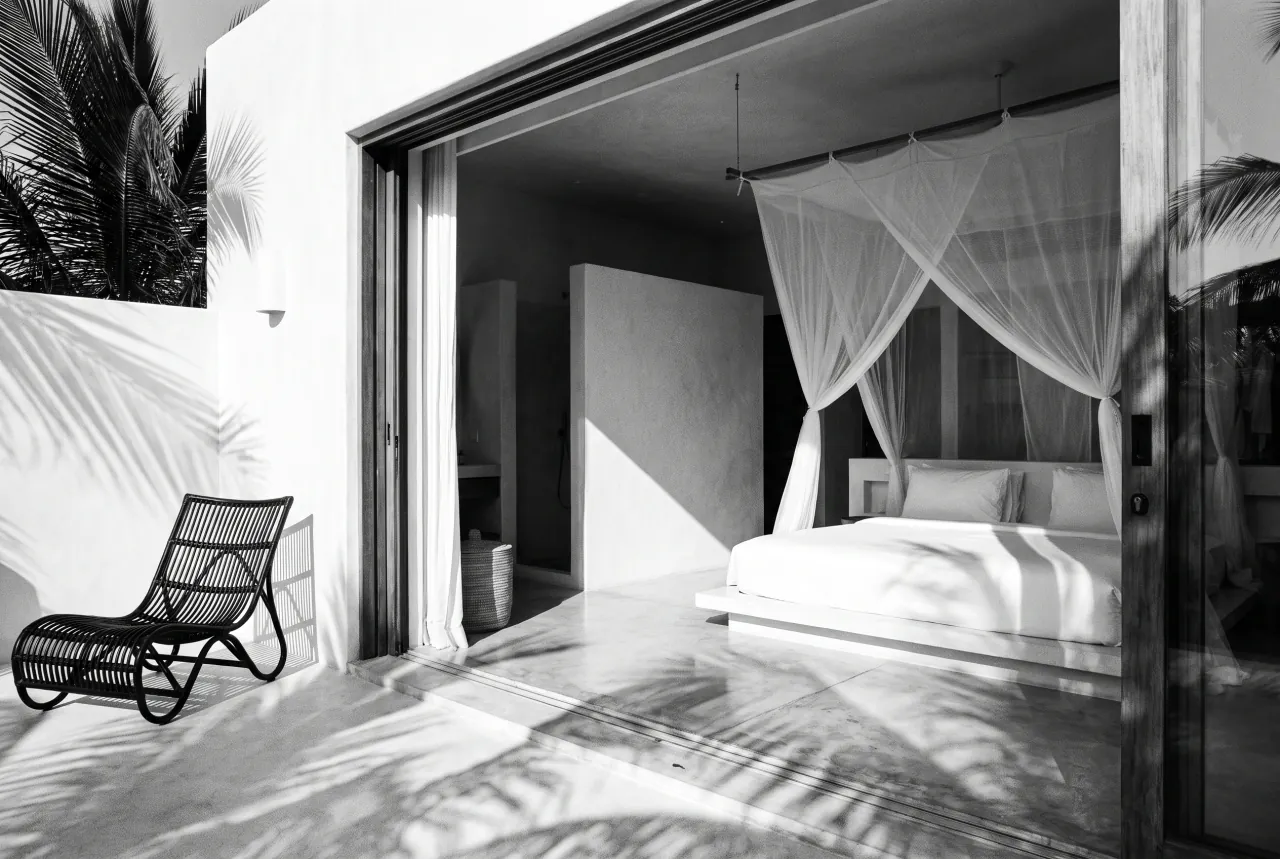 Baobab Studio at Black Groove Lounge — minimalist bedroom with mosquito net and open sliding doors to a palm garden, black and white photograph